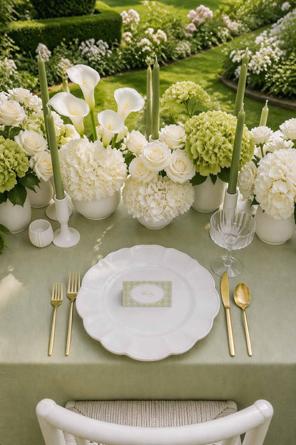 a beautifully set table with a white tablecloth, a white plate, and gold cutlery. The table is adorned with white flowers and candles, creating a serene and elegant atmosphere.