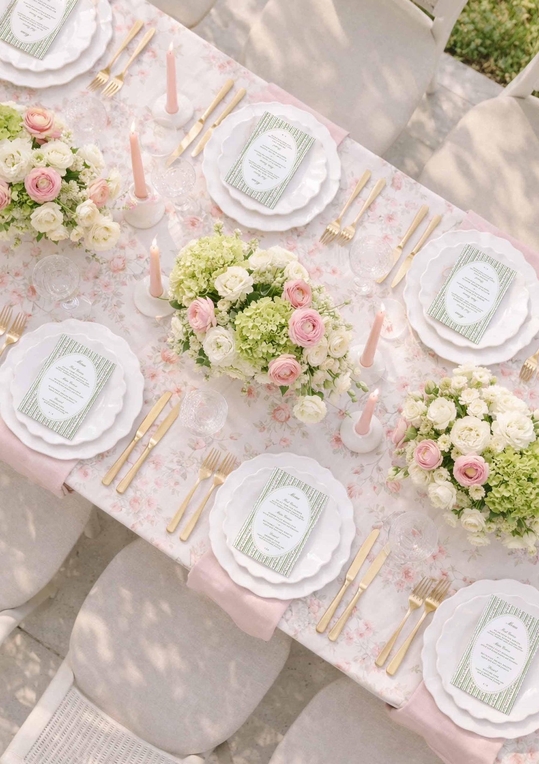a beautifully set dining table with white plates, gold cutlery, and a floral centerpiece. The table is adorned with pink and white flowers, creating a romantic and elegant atmosphere.
