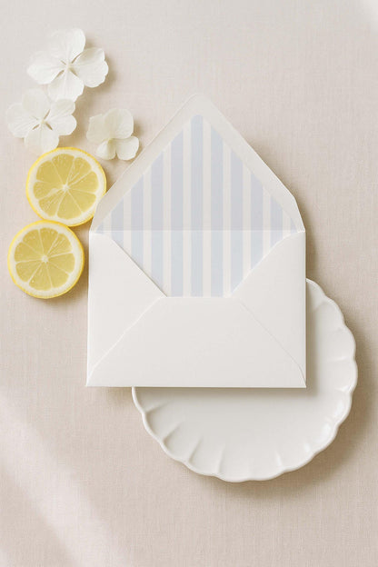 a white envelope with blue stripes, a white plate, and two lemon slices on a beige background.
