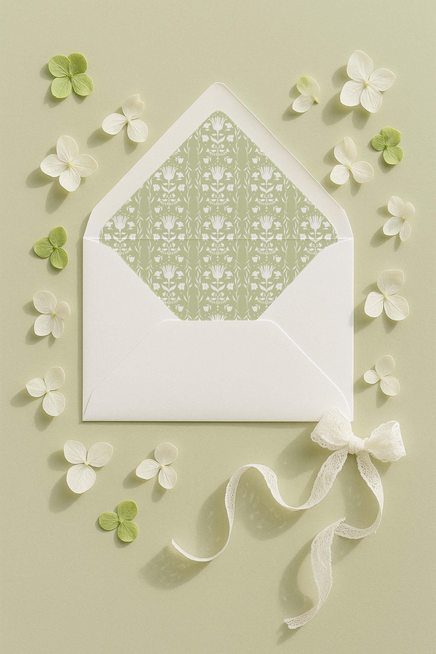 a white envelope with a green floral pattern, surrounded by white flowers and a white ribbon.