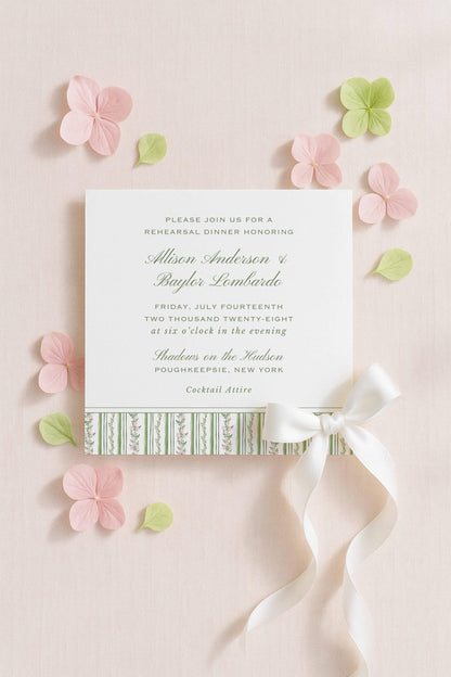 The image is a wedding invitation card with a white background, green and pink floral accents, and a white ribbon bow.