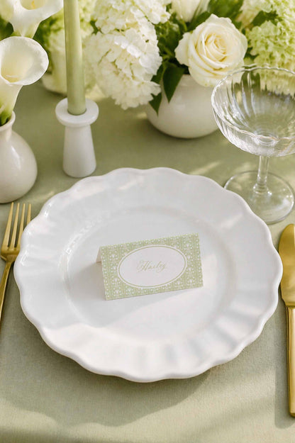 a beautifully set table with a white plate, a name card, and various tableware items such as a wine glass, a fork, and a knife.
