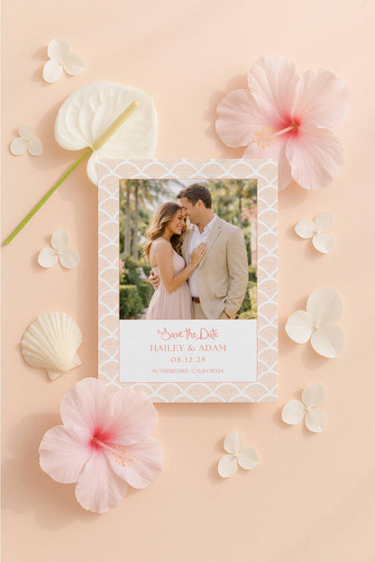 A wedding invitation featuring a couple embracing, surrounded by pink flowers and shells on a peach background.