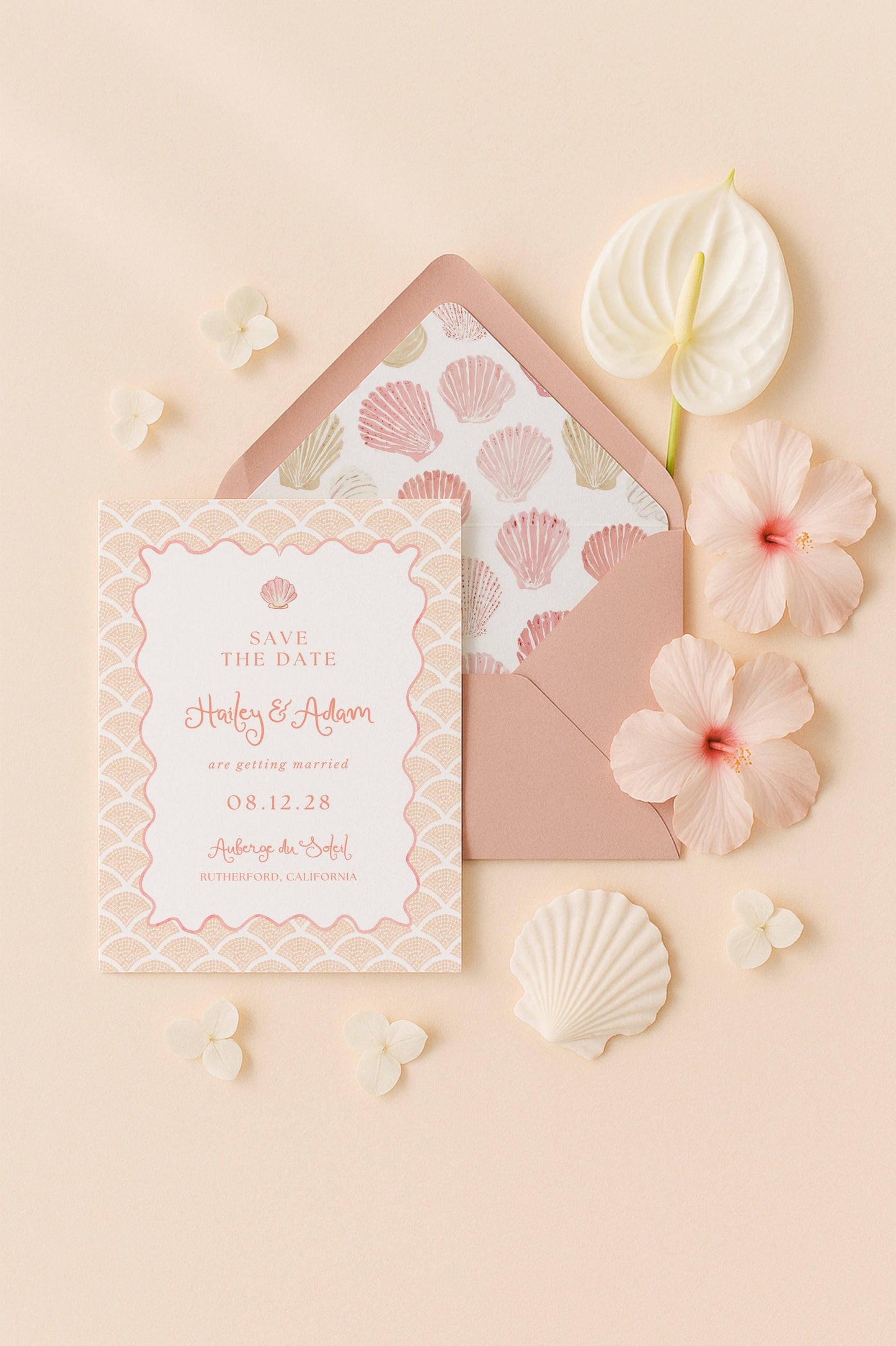 A pink and white wedding invitation card with the text "Save the Date" and "Harley & Adam are getting married 08.12.28" printed on it, along with a matching envelope, a white hibiscus flower, and some seashells.