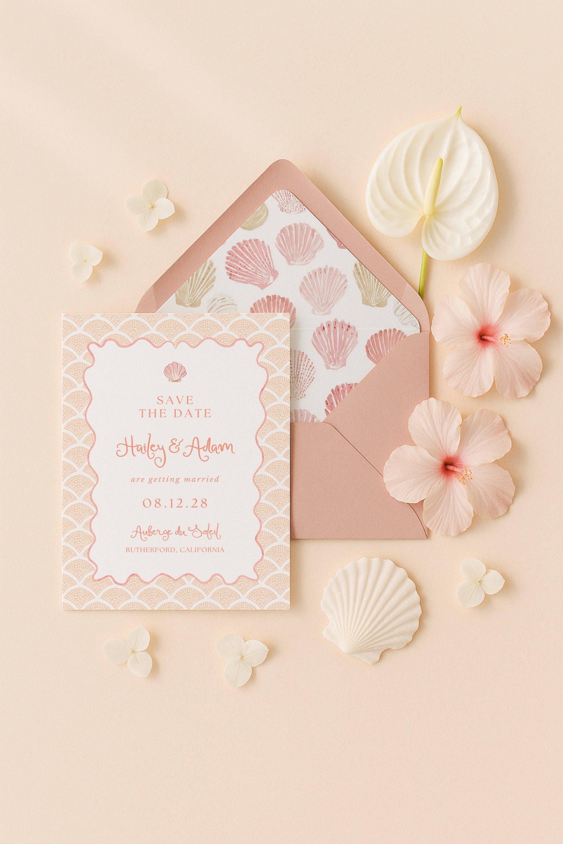 A pink and white wedding invitation card with the text "Save the Date" and "Harley & Adam are getting married 08.12.28" printed on it, along with a matching envelope, a white hibiscus flower, and some seashells.