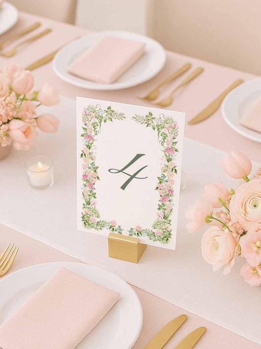 "Floral watercolor table number card displayed on an elegant pink and gold wedding tablescape with soft blush flowers and gold flatware."