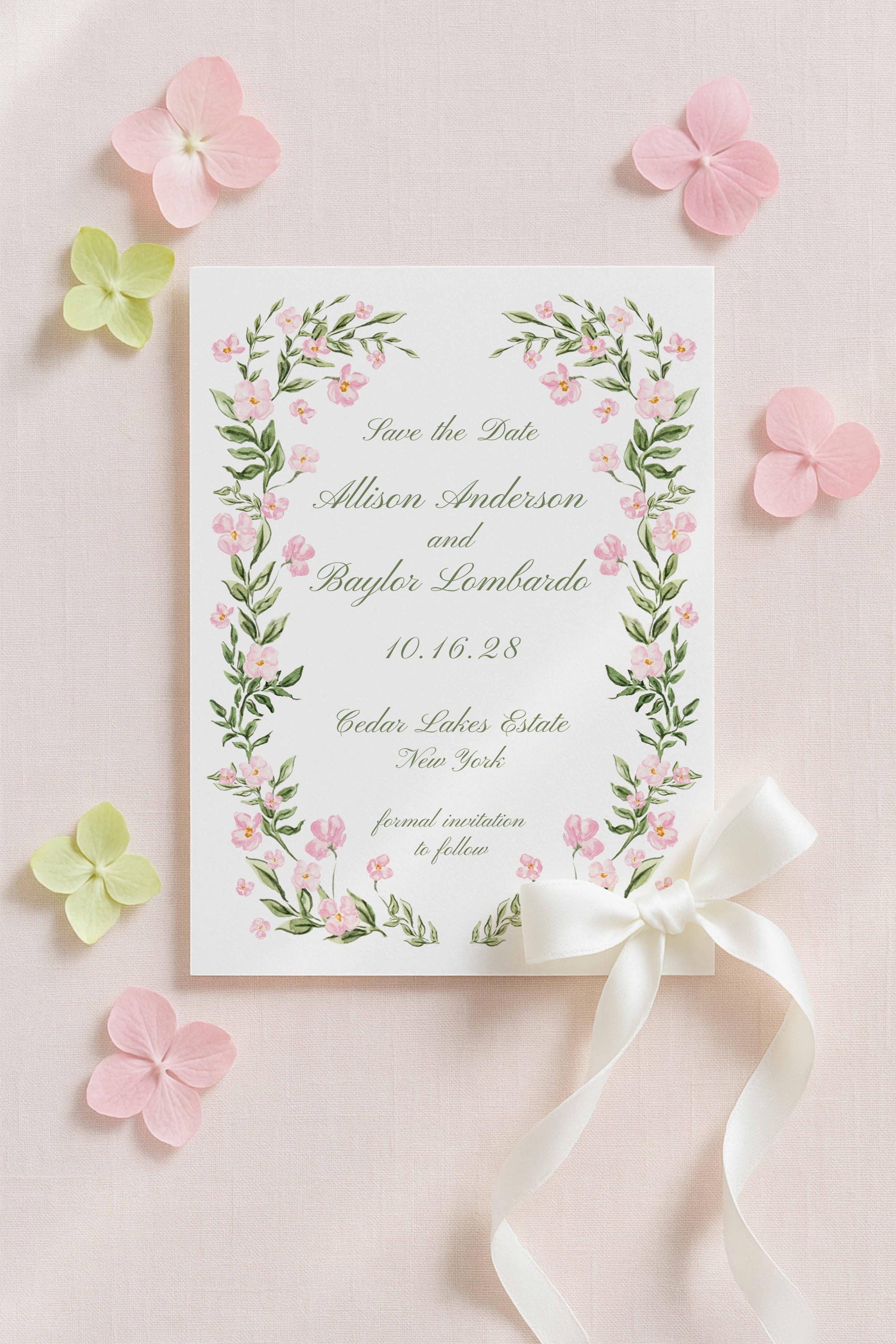 a white card with a floral border and a white ribbon, surrounded by pink and green flowers on a light pink background.