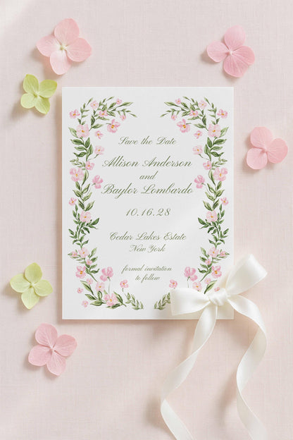 a white card with a floral border and a white ribbon, surrounded by pink and green flowers on a light pink background.