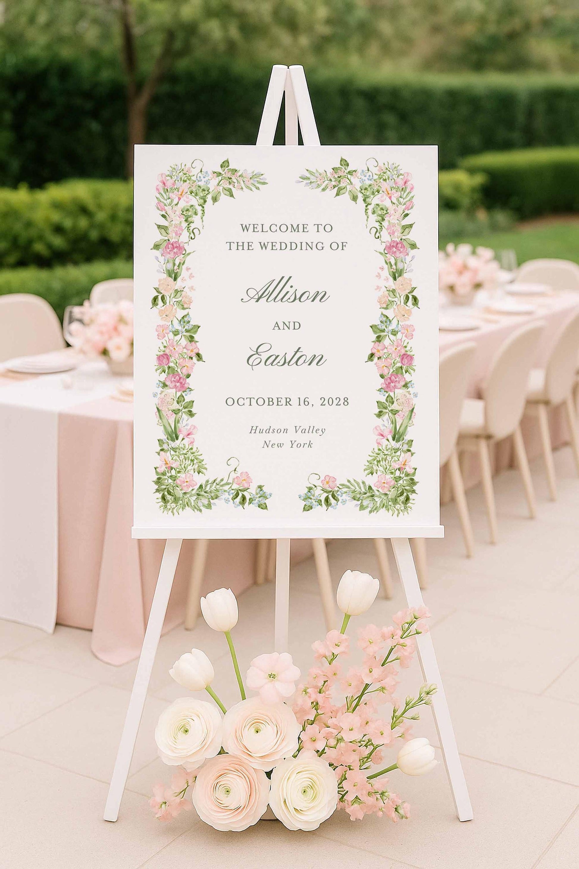 Editable watercolor floral wedding welcome sign on an easel beside pastel flowers at an elegant outdoor ceremony.