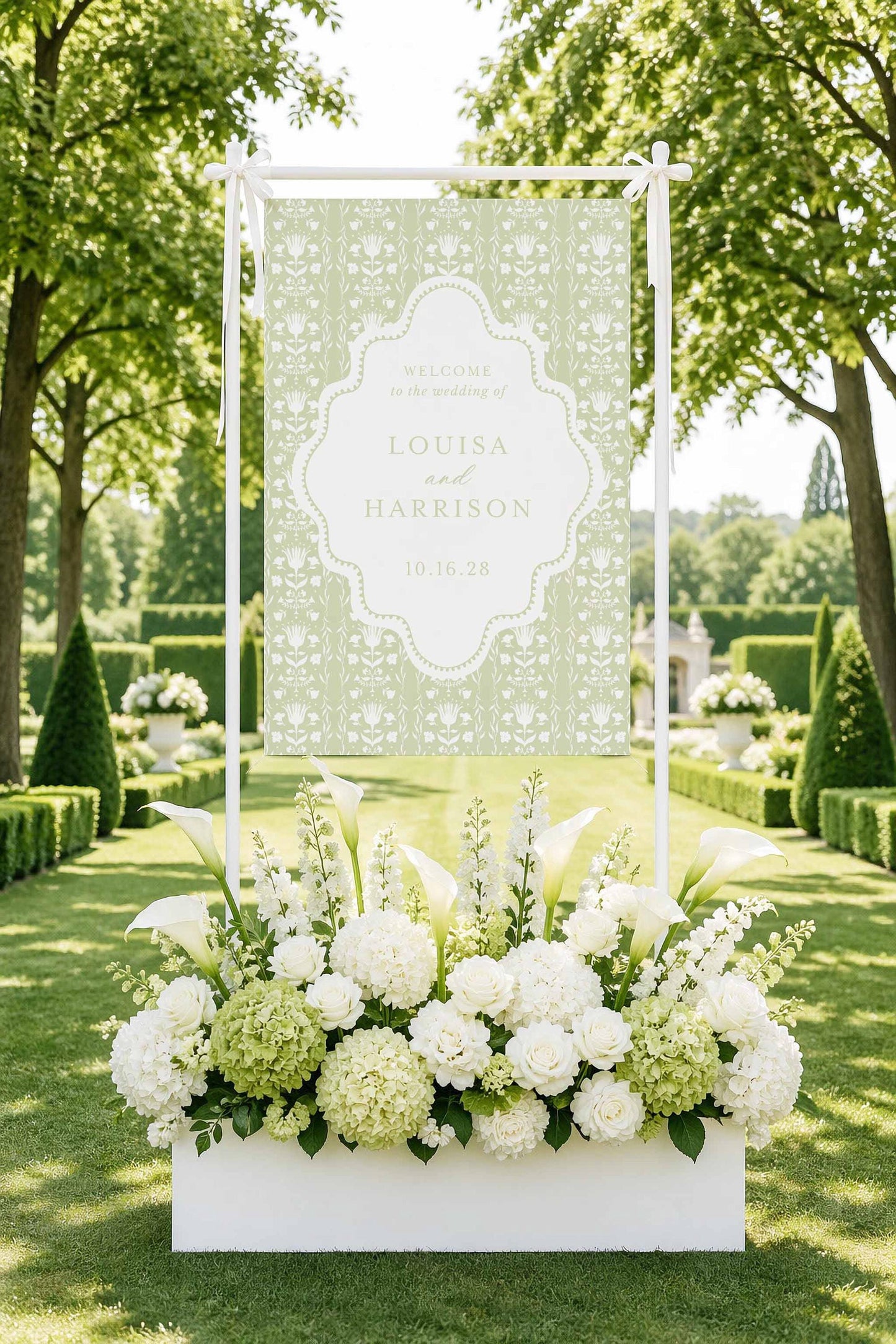 a large white banner with a floral design, surrounded by a beautiful arrangement of white flowers in a white box, set against a backdrop of lush greenery and trees.