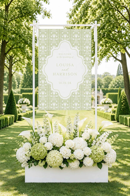 a large white banner with a floral design, surrounded by a beautiful arrangement of white flowers in a white box, set against a backdrop of lush greenery and trees.