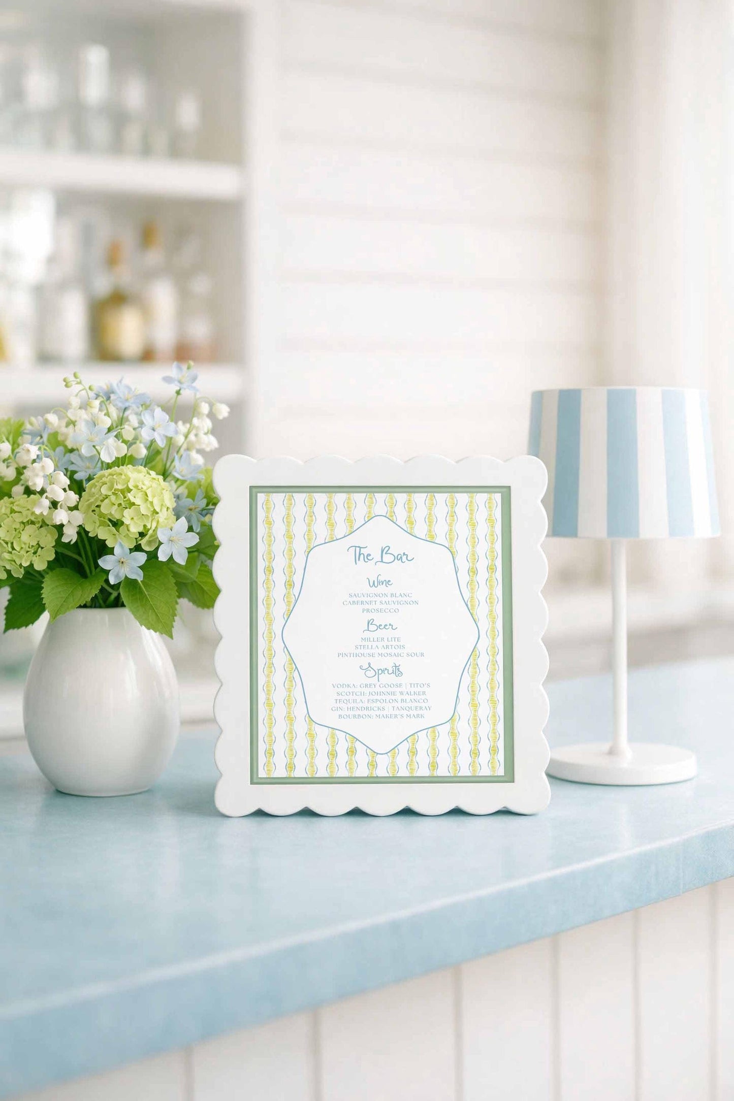 a white framed menu with a green and white striped border, placed on a blue countertop next to a vase of white flowers and a white lamp.