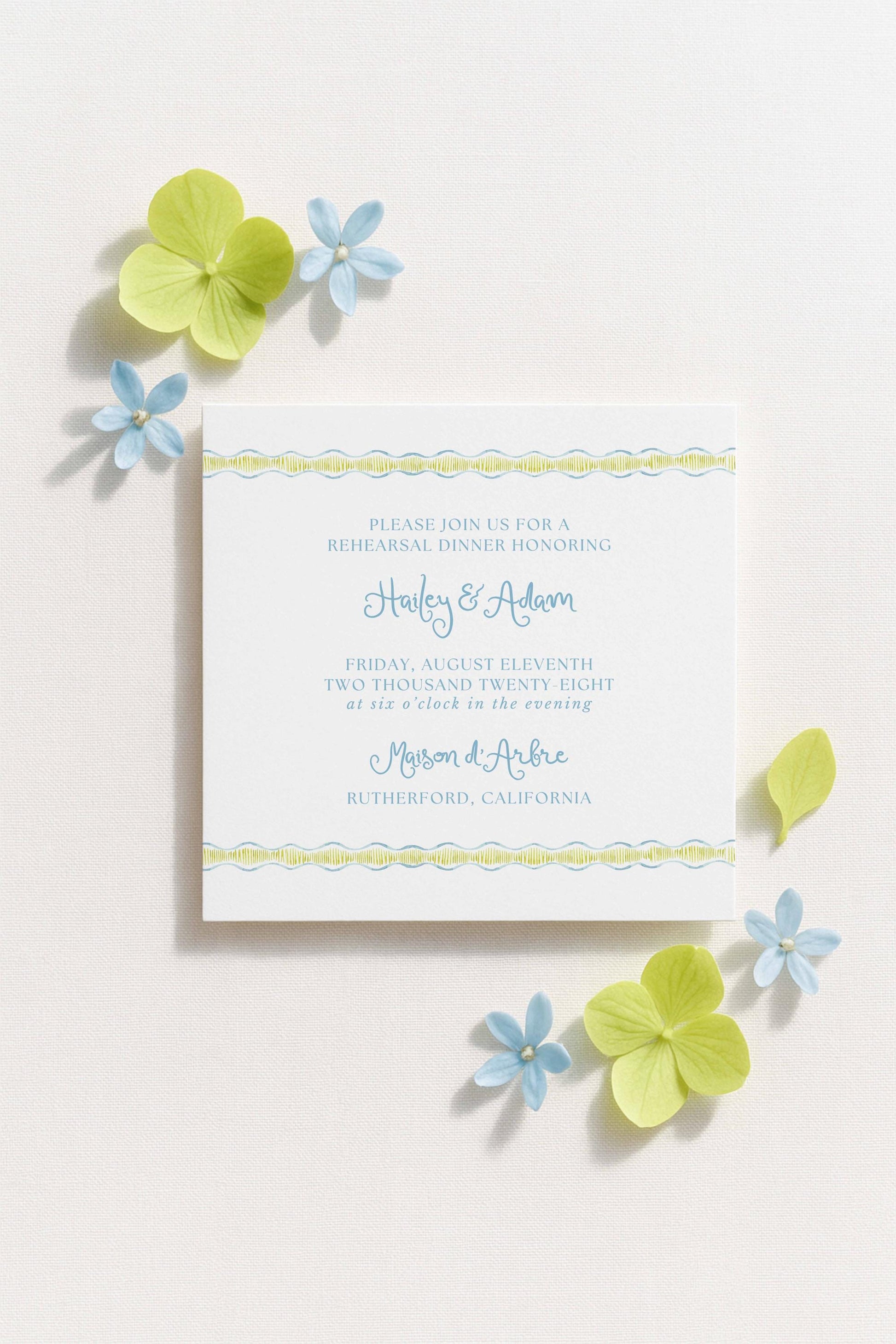 The image is a wedding invitation card with a white background, blue and green accents, and a floral border.