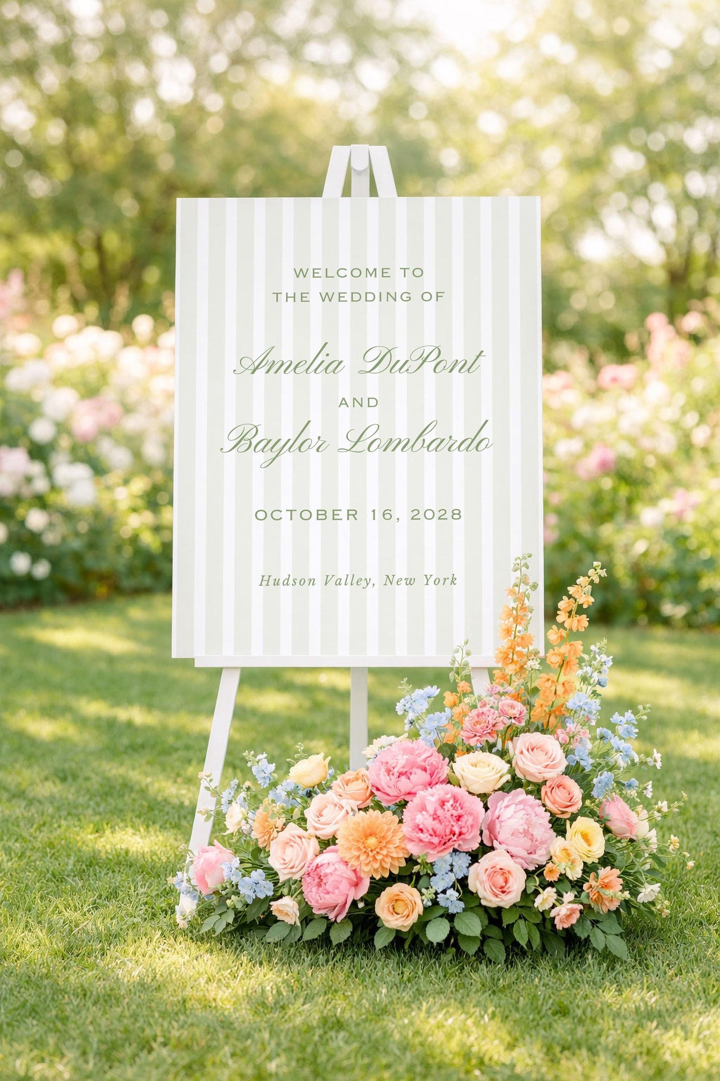 a white wedding sign with a floral arrangement in front of it, set against a backdrop of greenery and flowers.