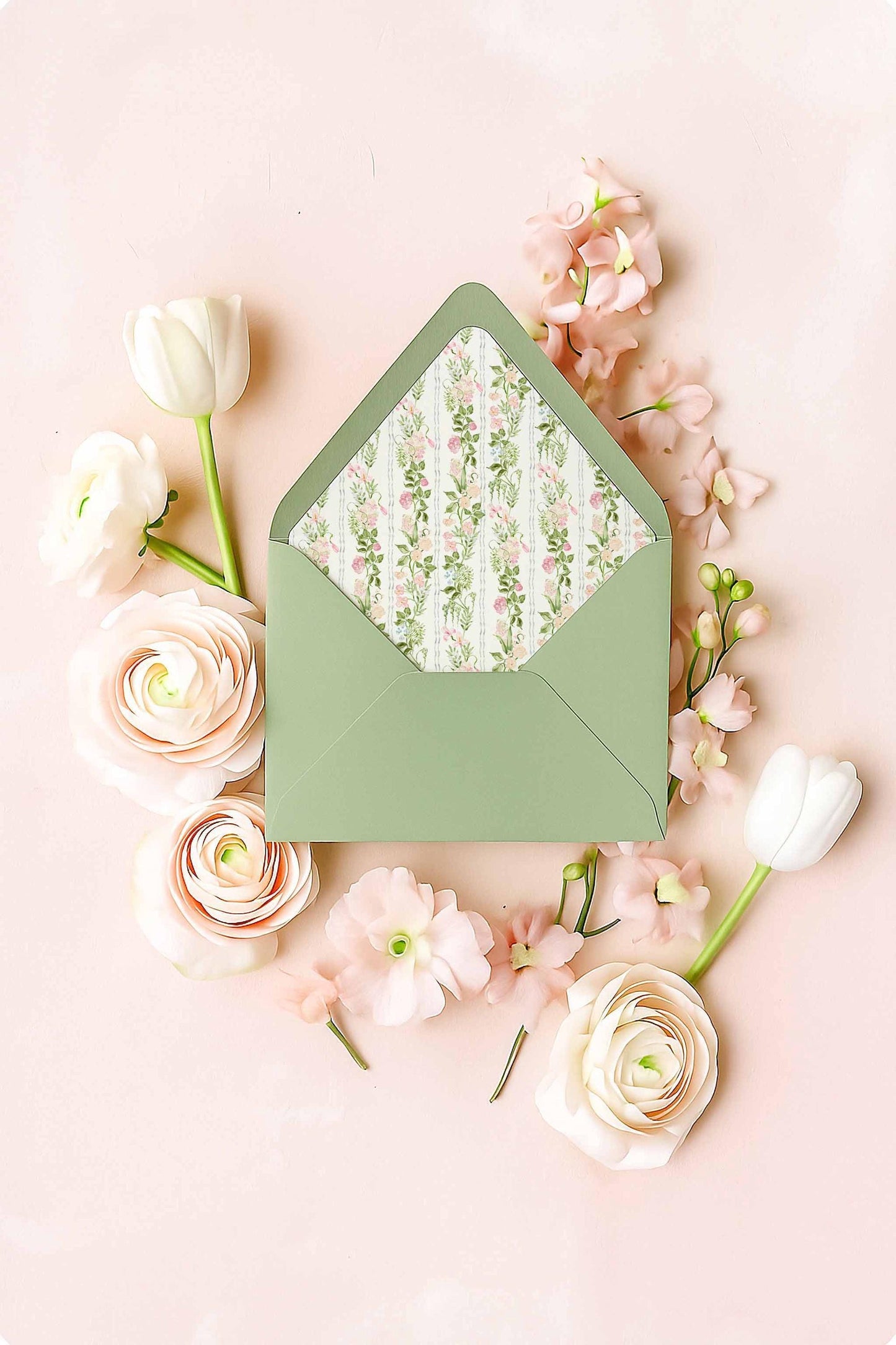 Green envelope with a floral watercolor envelope liner featuring hand-painted pink and green flowers, displayed in a flat lay with soft blush ranunculus, tulips, and florals on a pastel pink background.