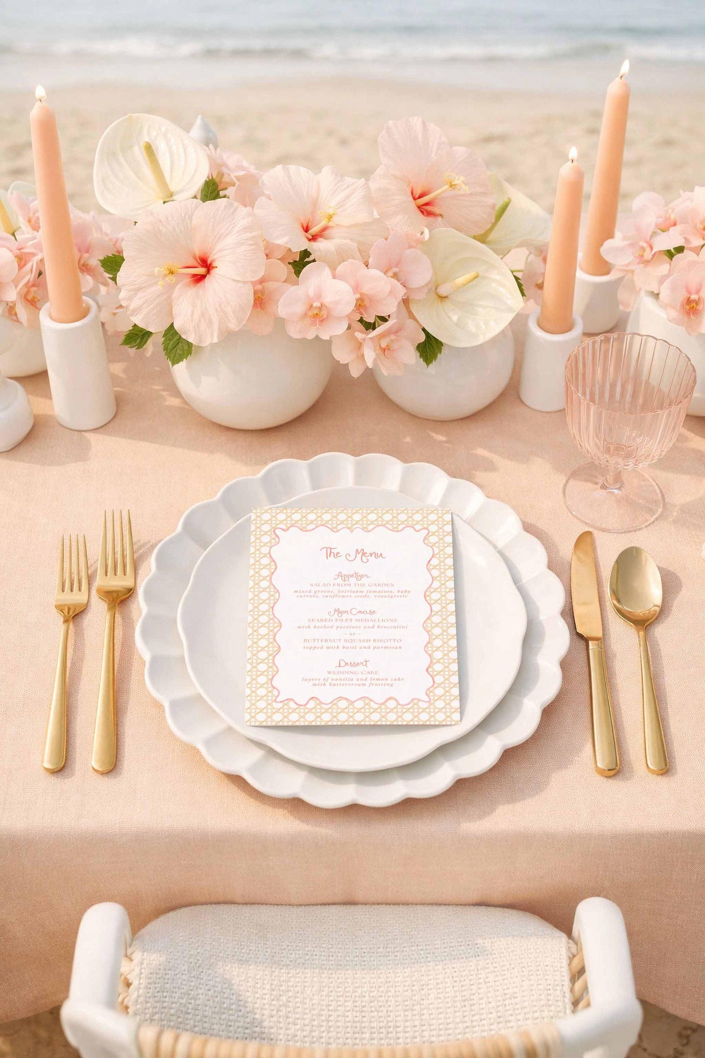 a beautifully set table with a white tablecloth, gold-colored plates, and a menu card. The table is adorned with pink flowers, candles, and glassware, creating an elegant and inviting atmosphere.