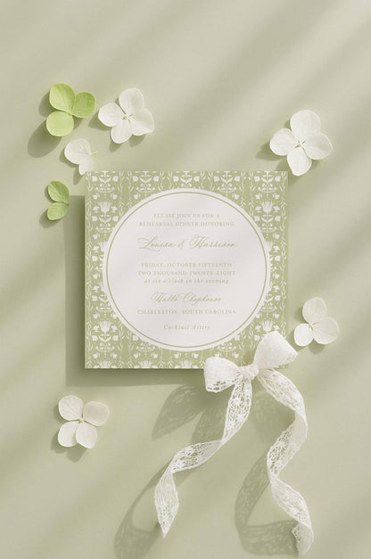 a wedding invitation card with a floral design, surrounded by white flowers and a white ribbon.