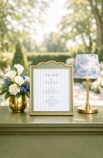 a framed menu with a decorative blue and white lamp on a table, surrounded by a vase of white and blue flowers.