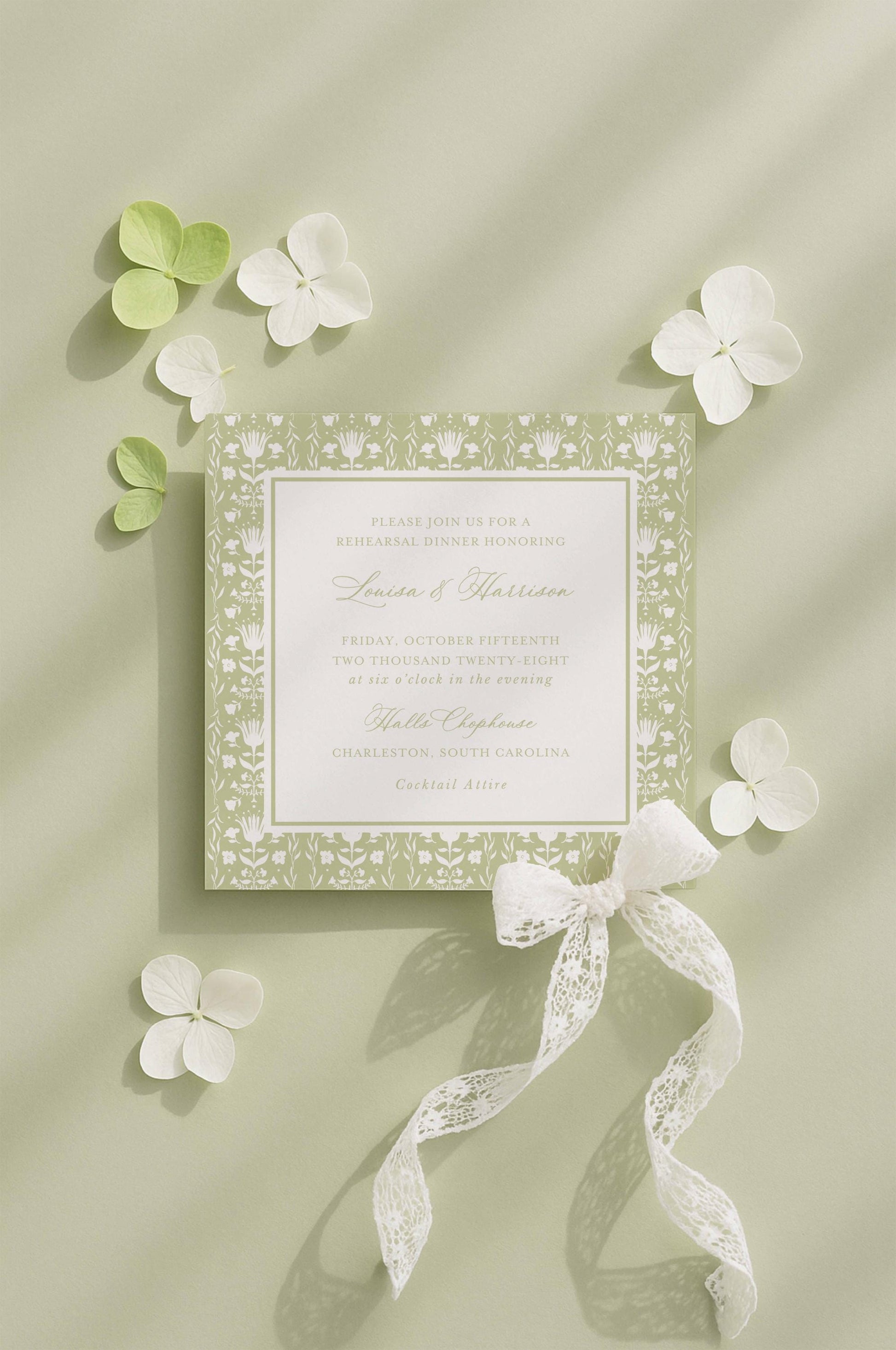 a wedding invitation card with a floral design, surrounded by white flowers and a white ribbon.
