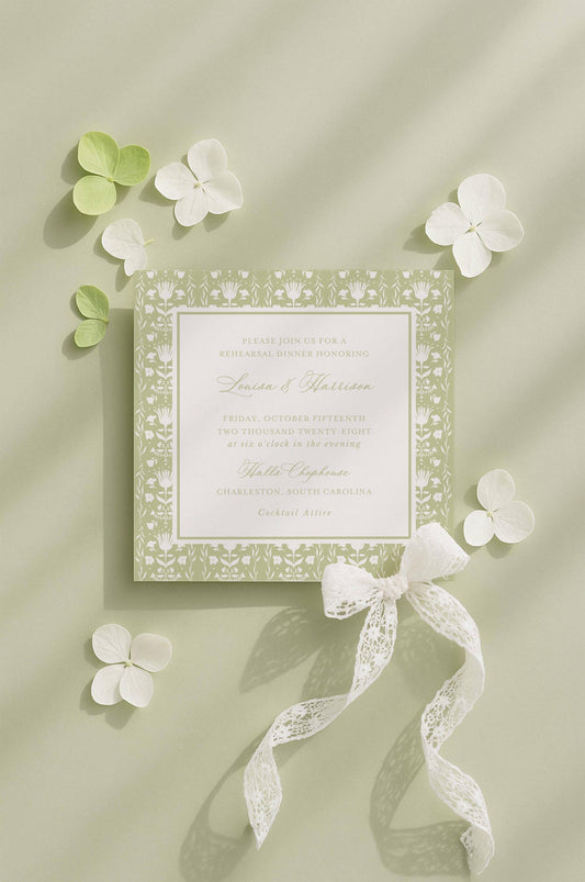 a wedding invitation card with a floral design, surrounded by white flowers and a white ribbon.