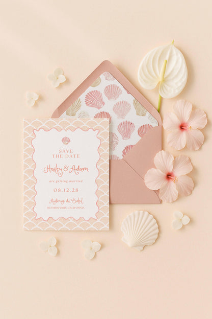 A pink and white wedding invitation card with the text "Save the Date" and "Harley & Adam are getting married 08.12.28" printed on it, along with a matching envelope, a white hibiscus flower, and some seashells.