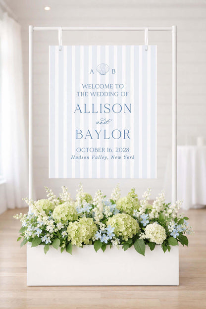 a wedding invitation sign with a floral arrangement in a white planter below it.