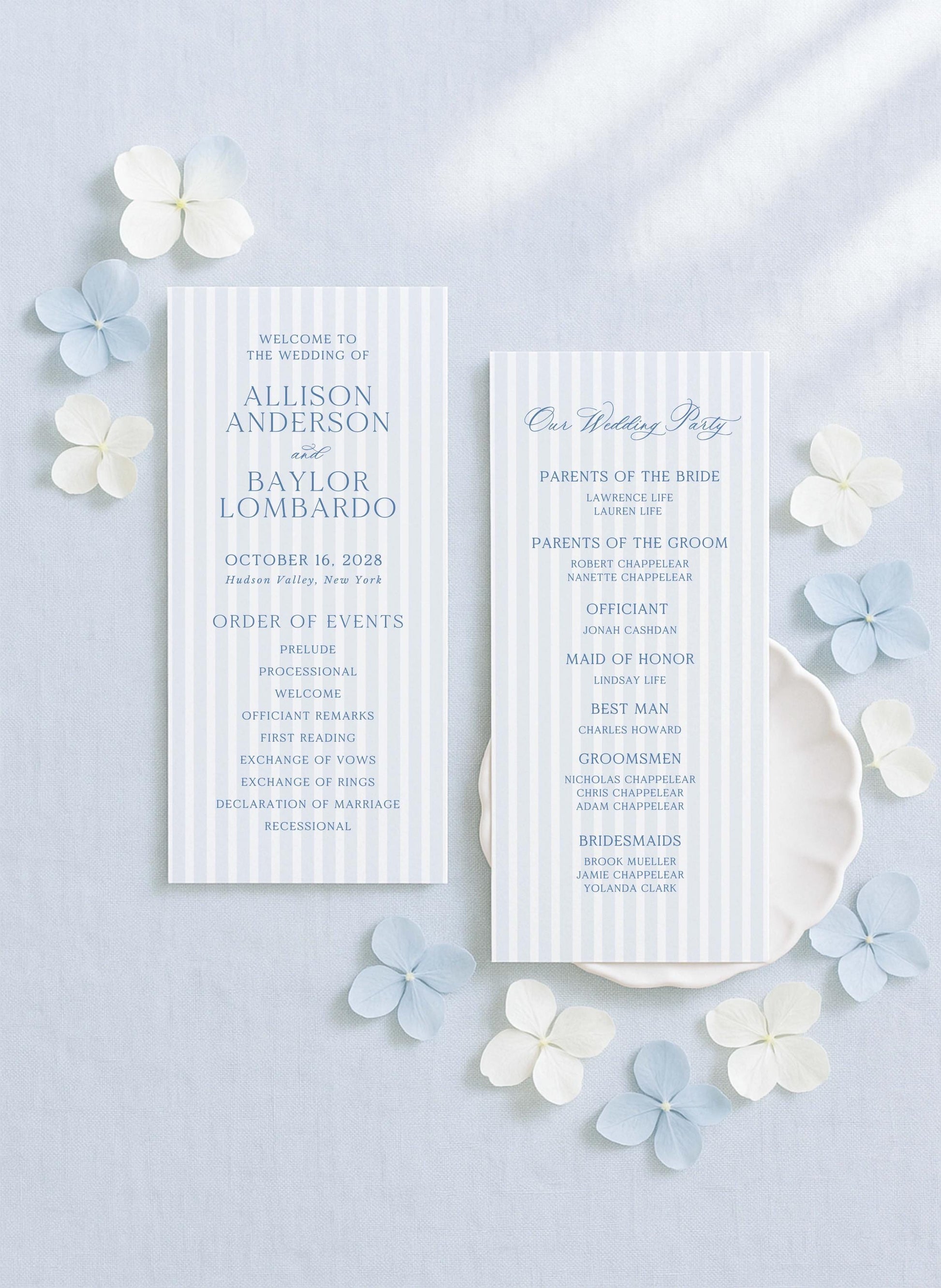 two white wedding invitation cards with blue and white stripes, placed on a light blue background with white and light blue flowers scattered around them.
