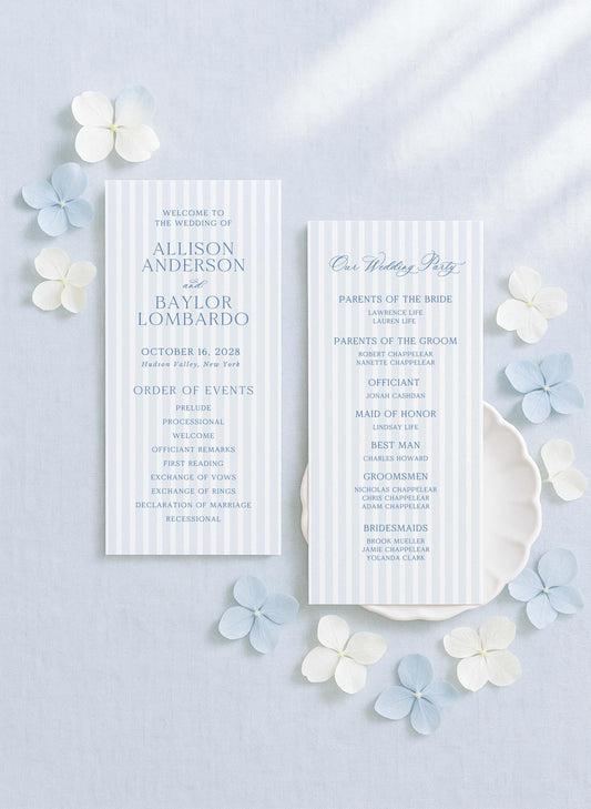 two white wedding invitation cards with blue and white stripes, placed on a light blue background with white and light blue flowers scattered around them.