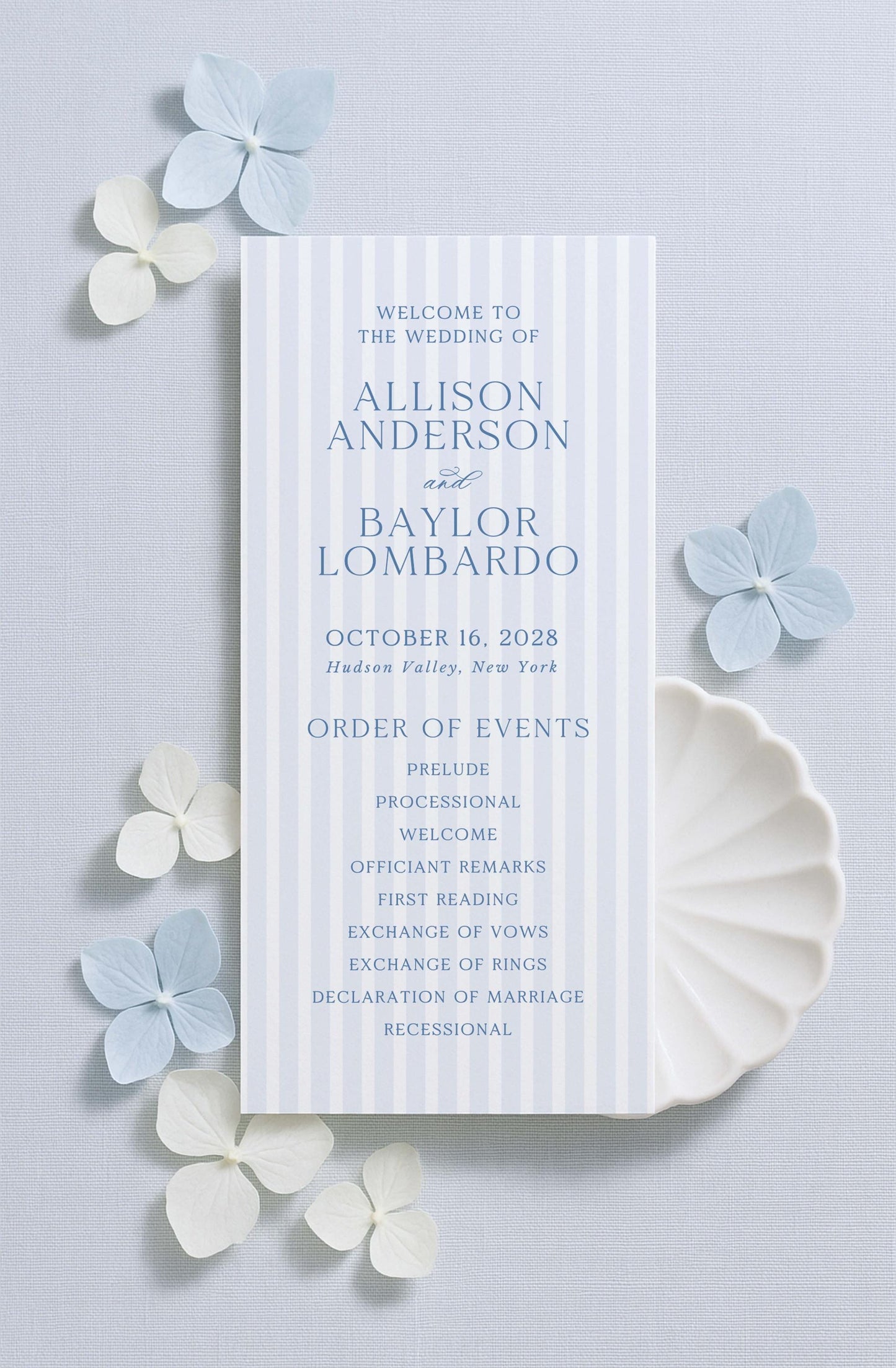 a wedding invitation card with a blue and white color scheme, placed on a light blue background with white flowers scattered around it.