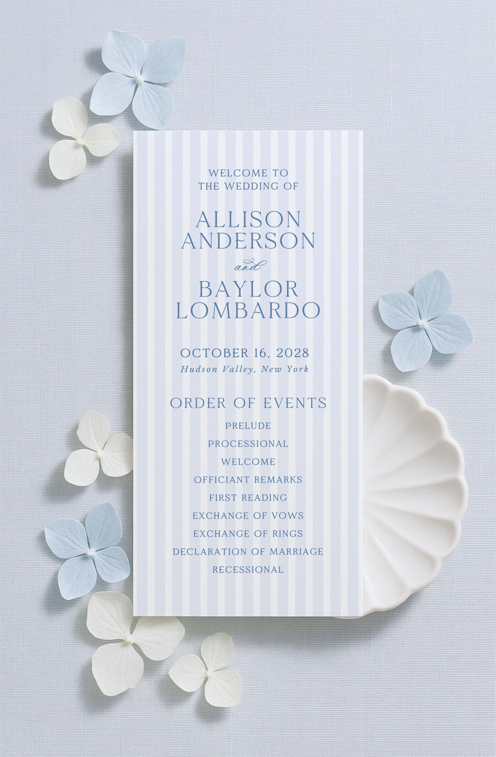 a wedding invitation card with a blue and white color scheme, placed on a light blue background with white flowers scattered around it.