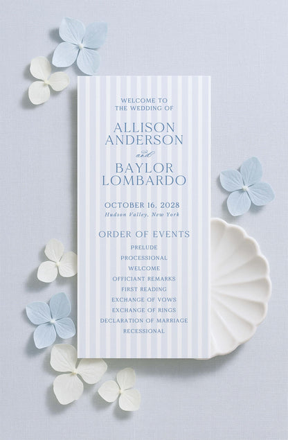 a wedding invitation card with a blue and white color scheme, placed on a light blue background with white flowers scattered around it.