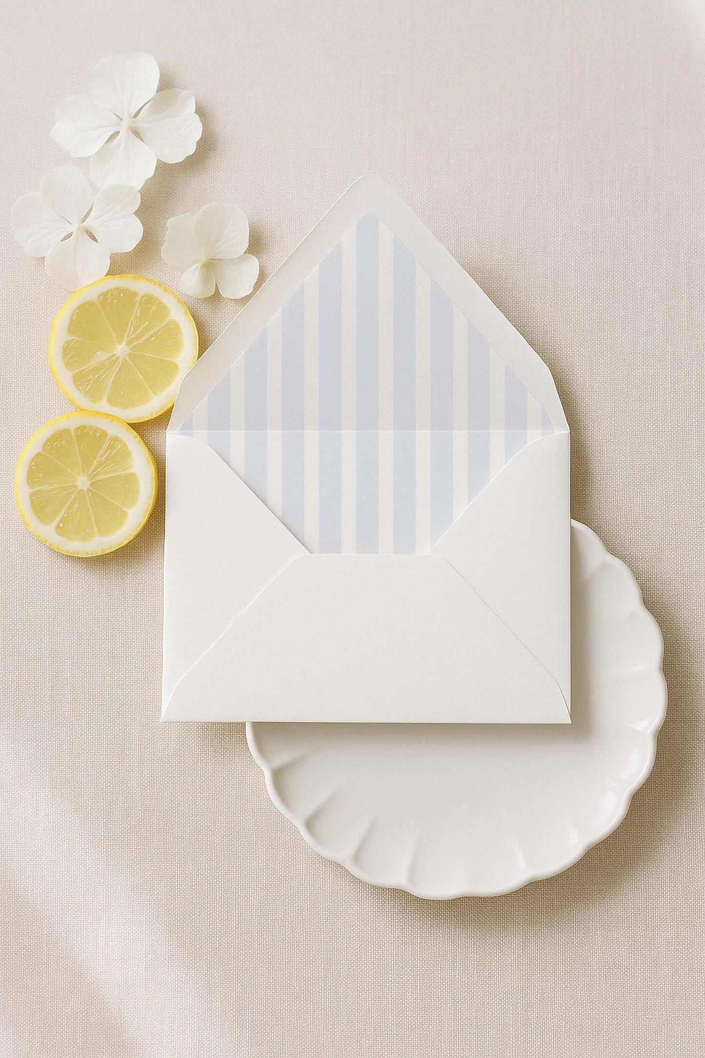 a white envelope with blue stripes, a white plate, and two lemon slices on a beige background.