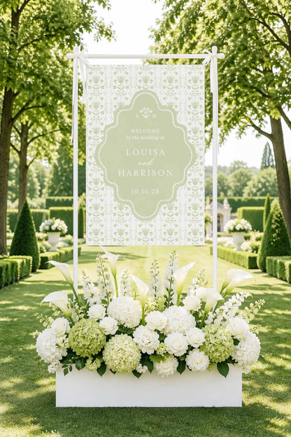 A white banner with floral arrangements in the foreground, set against a backdrop of lush greenery and trees.