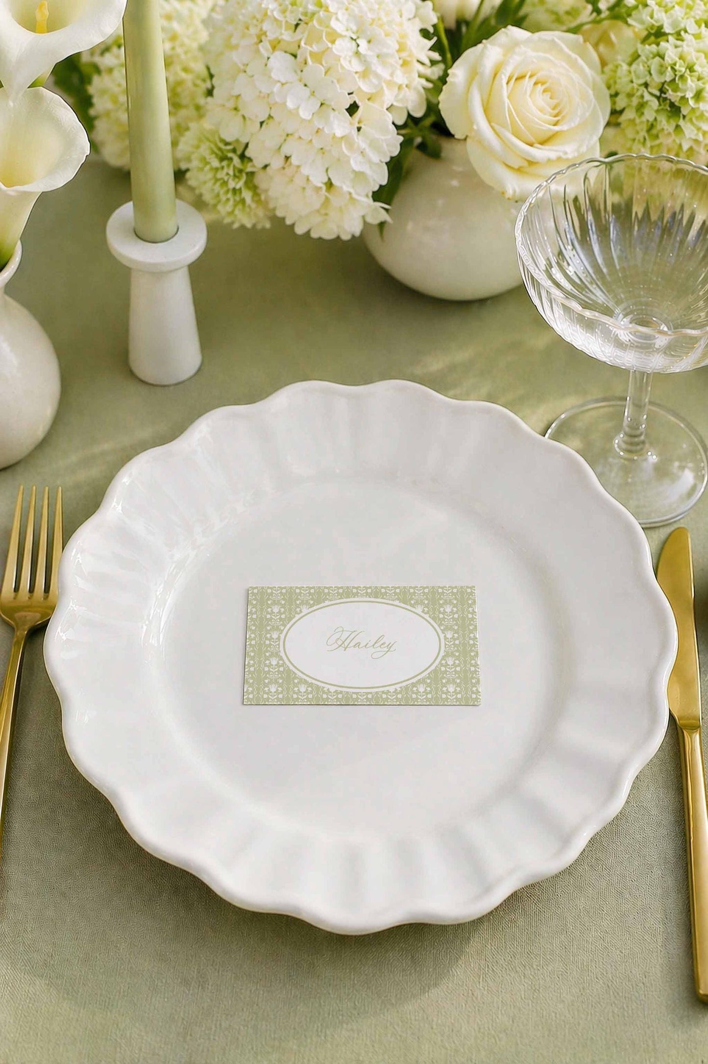 a table setting with a white plate, a glass of wine, a vase of white flowers, and a candle. The table is set for a formal dining experience.
