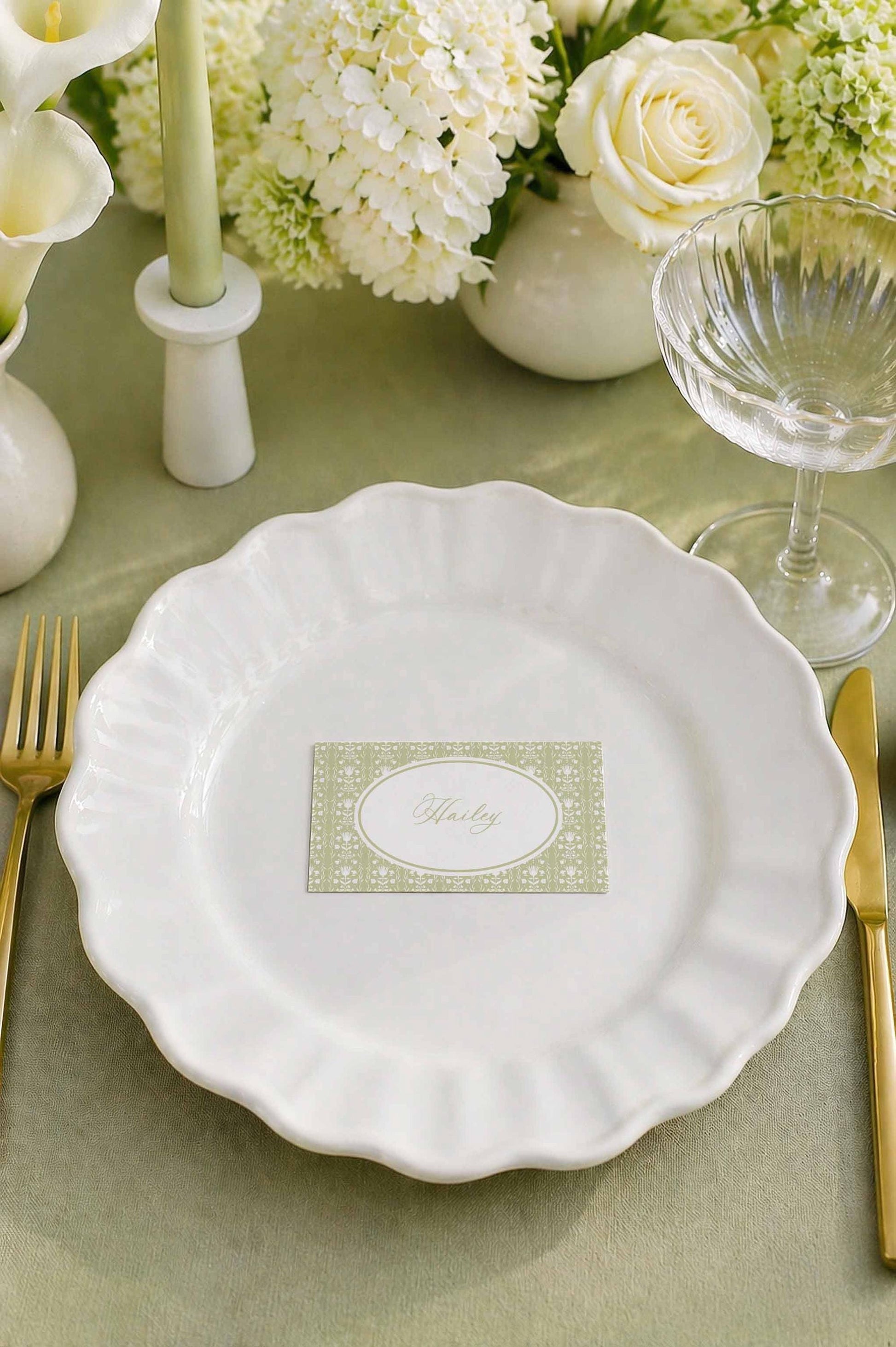 a table setting with a white plate, a glass of wine, a vase of white flowers, and a candle. The table is set for a formal dining experience.