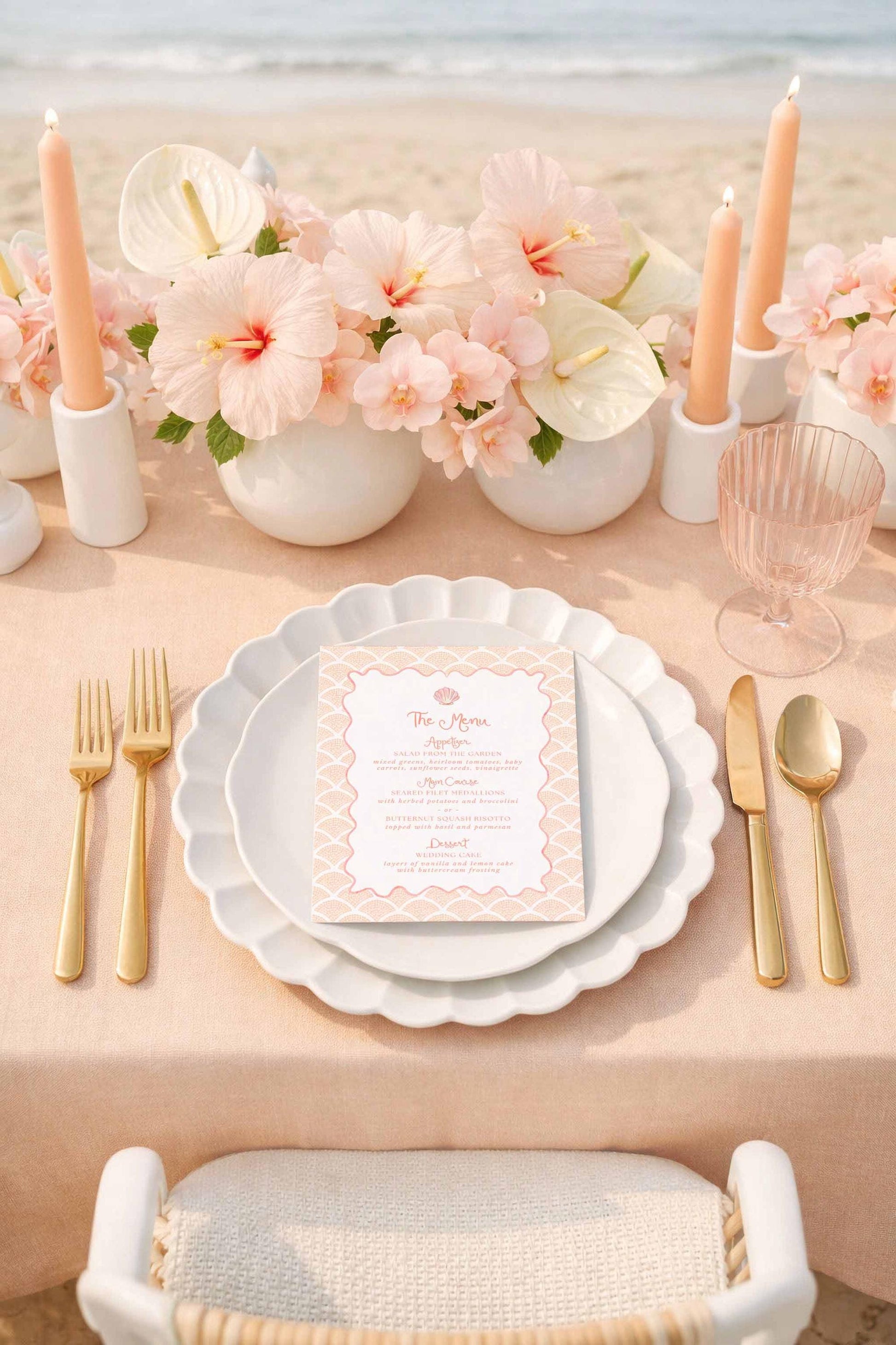 a beautifully set table with a pink tablecloth, featuring a menu card, gold cutlery, and a vase of pink flowers. The table is set on a beach, with the ocean visible in the background.