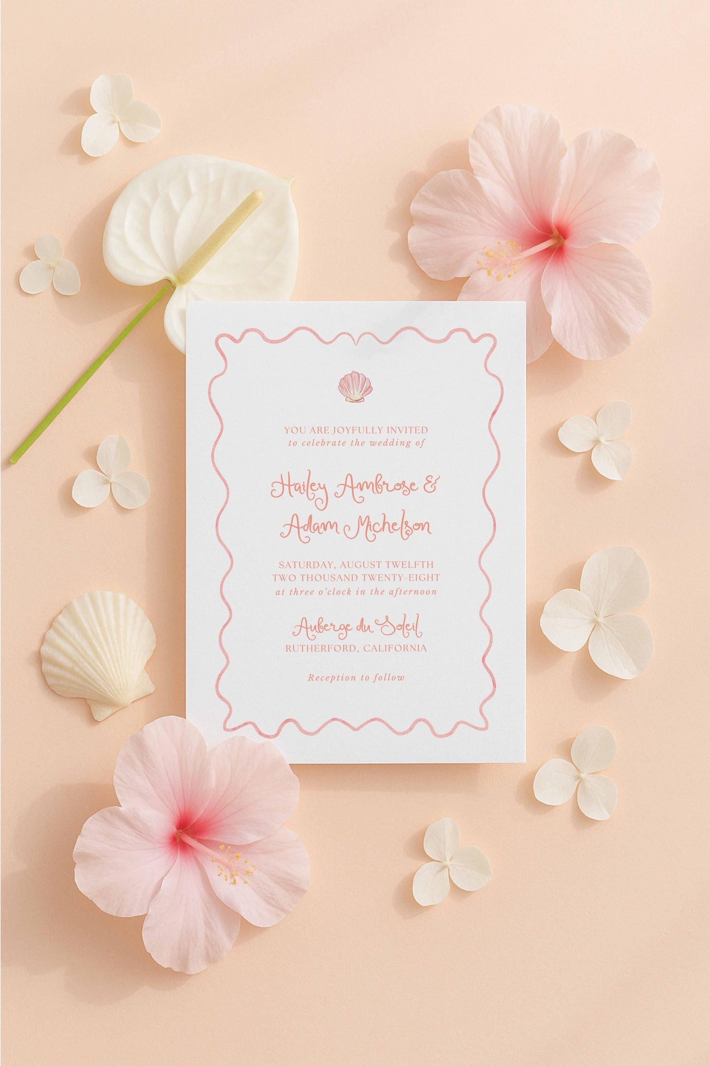 a wedding invitation card surrounded by various pink and white flowers, shells, and leaves, creating a beautiful and natural-themed setting.