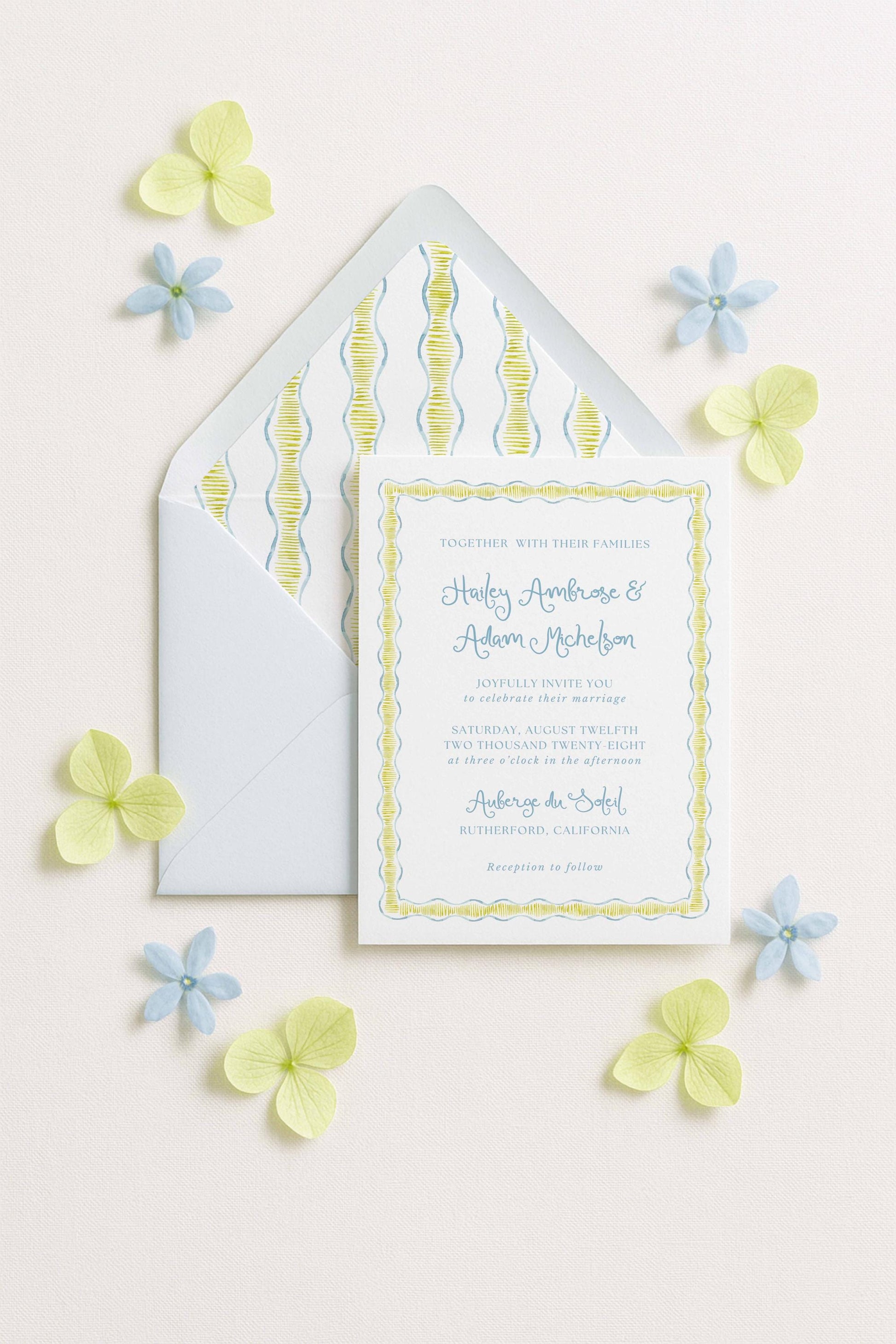 A wedding invitation card with a yellow and blue floral border, surrounded by small blue and yellow flowers on a light background.