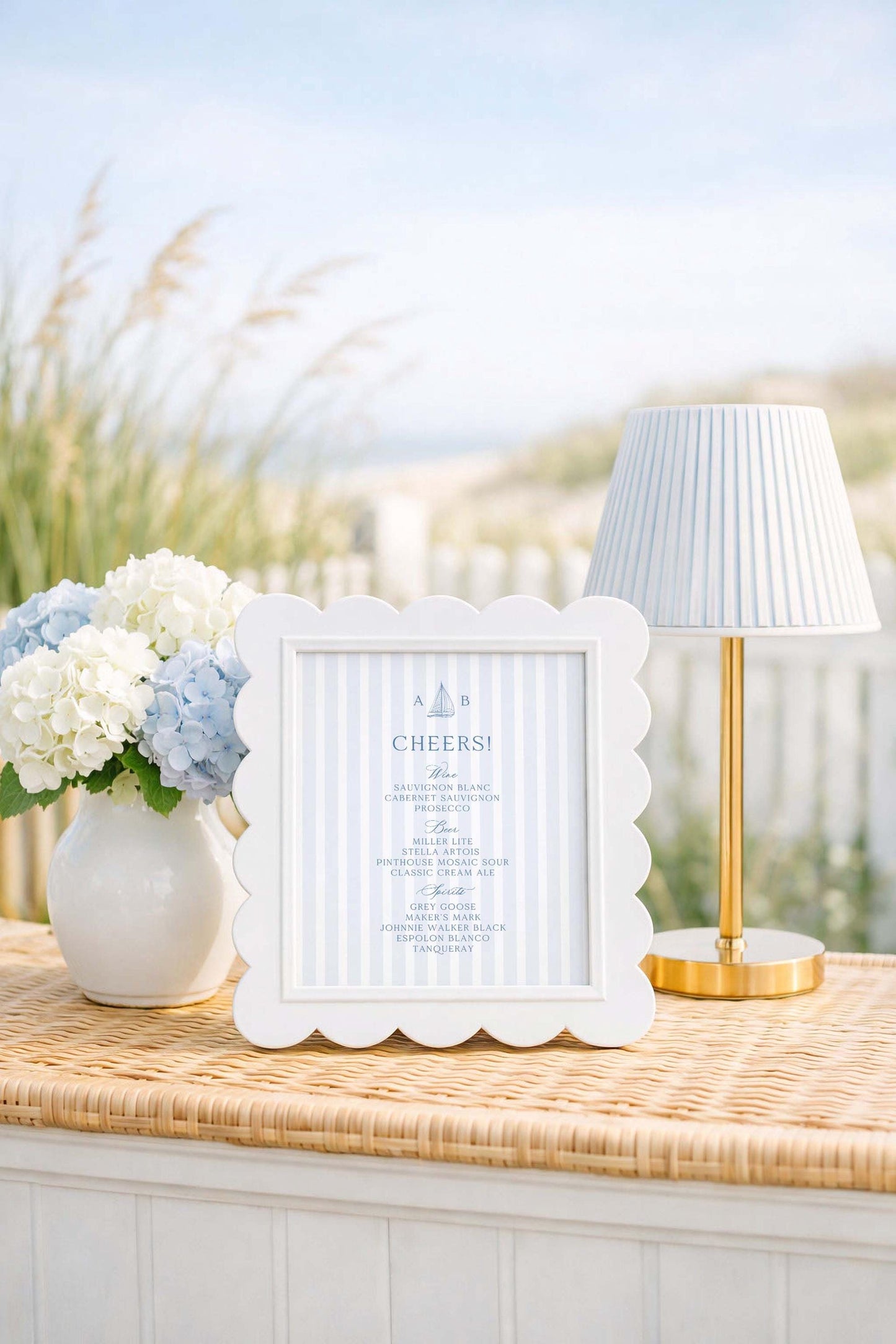 a white framed sign with blue text, a white vase with white and blue flowers, and a white lamp with a gold base, all placed on a woven table.