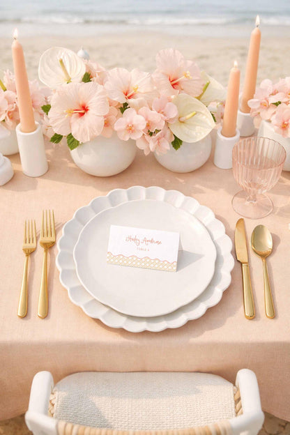 a beautifully set table with a pink tablecloth, featuring a white plate, gold cutlery, and a card. The table is adorned with pink flowers and candles, creating a romantic and elegant atmosphere.