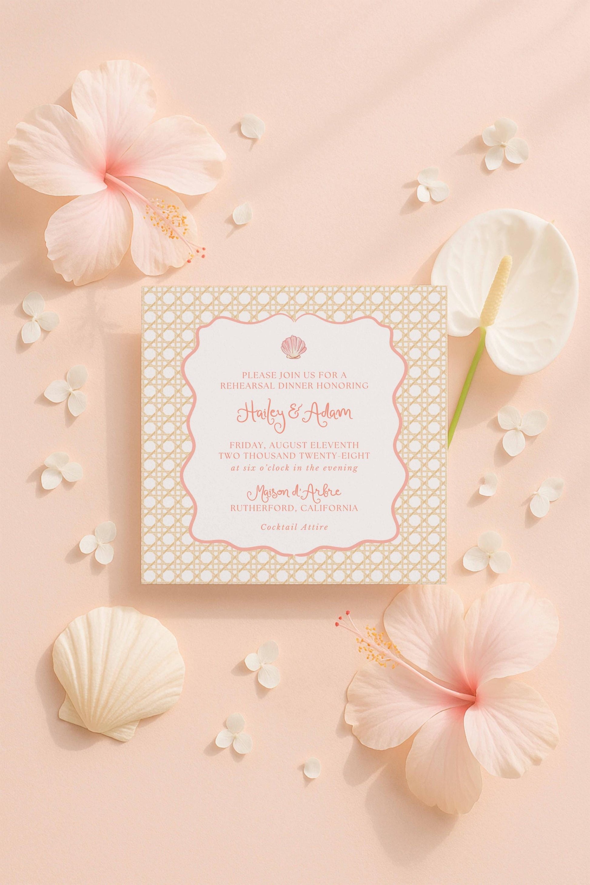 a wedding invitation card with a floral design, surrounded by pink hibiscus flowers, seashells, and other decorative elements on a peach-colored background.