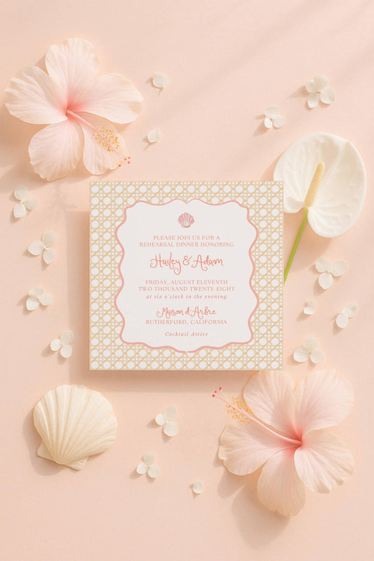 a wedding invitation card with a floral design, surrounded by pink hibiscus flowers, seashells, and other decorative elements on a peach-colored background.