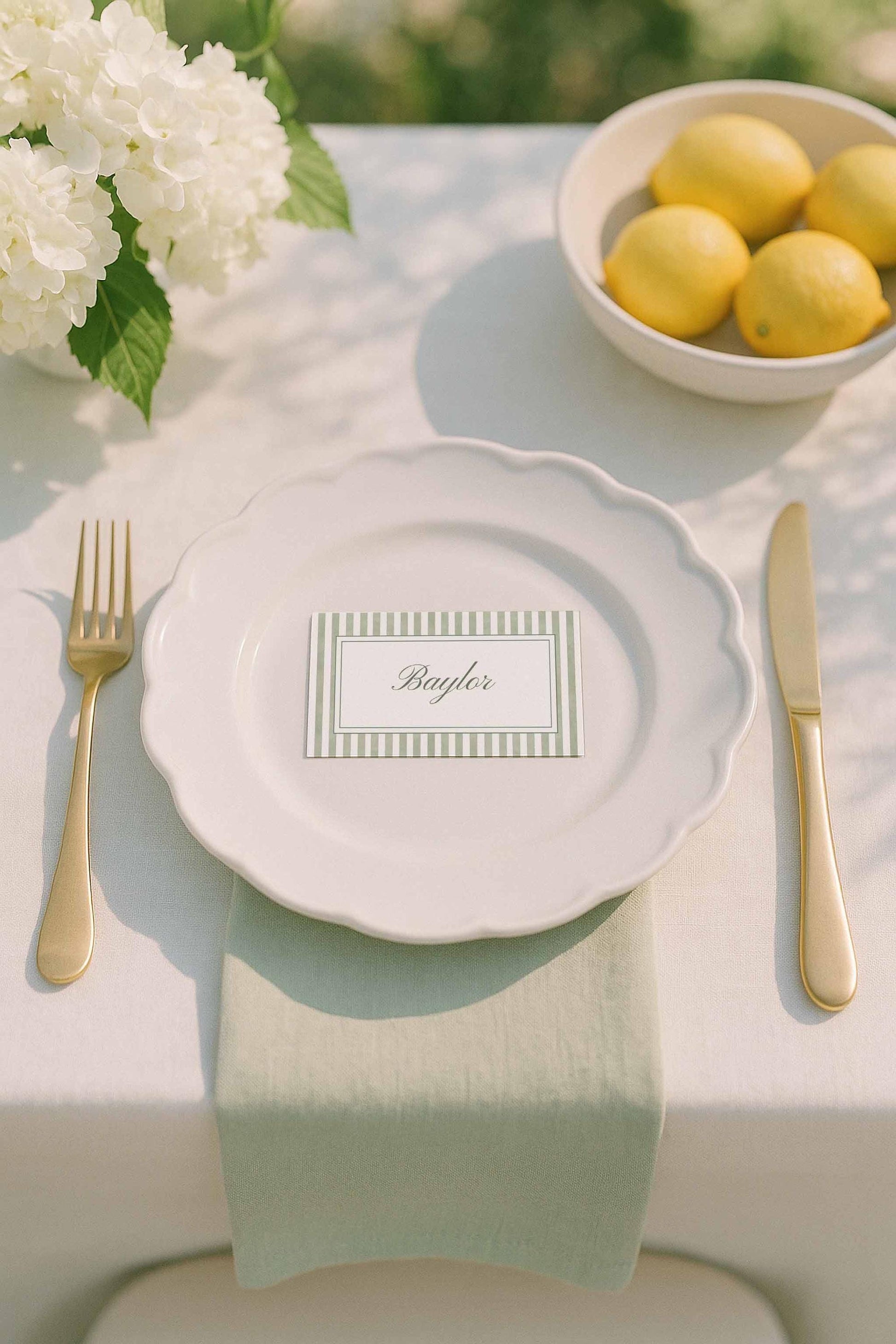 Green striped wedding name card displayed on a place setting with soft florals and gold flatware.