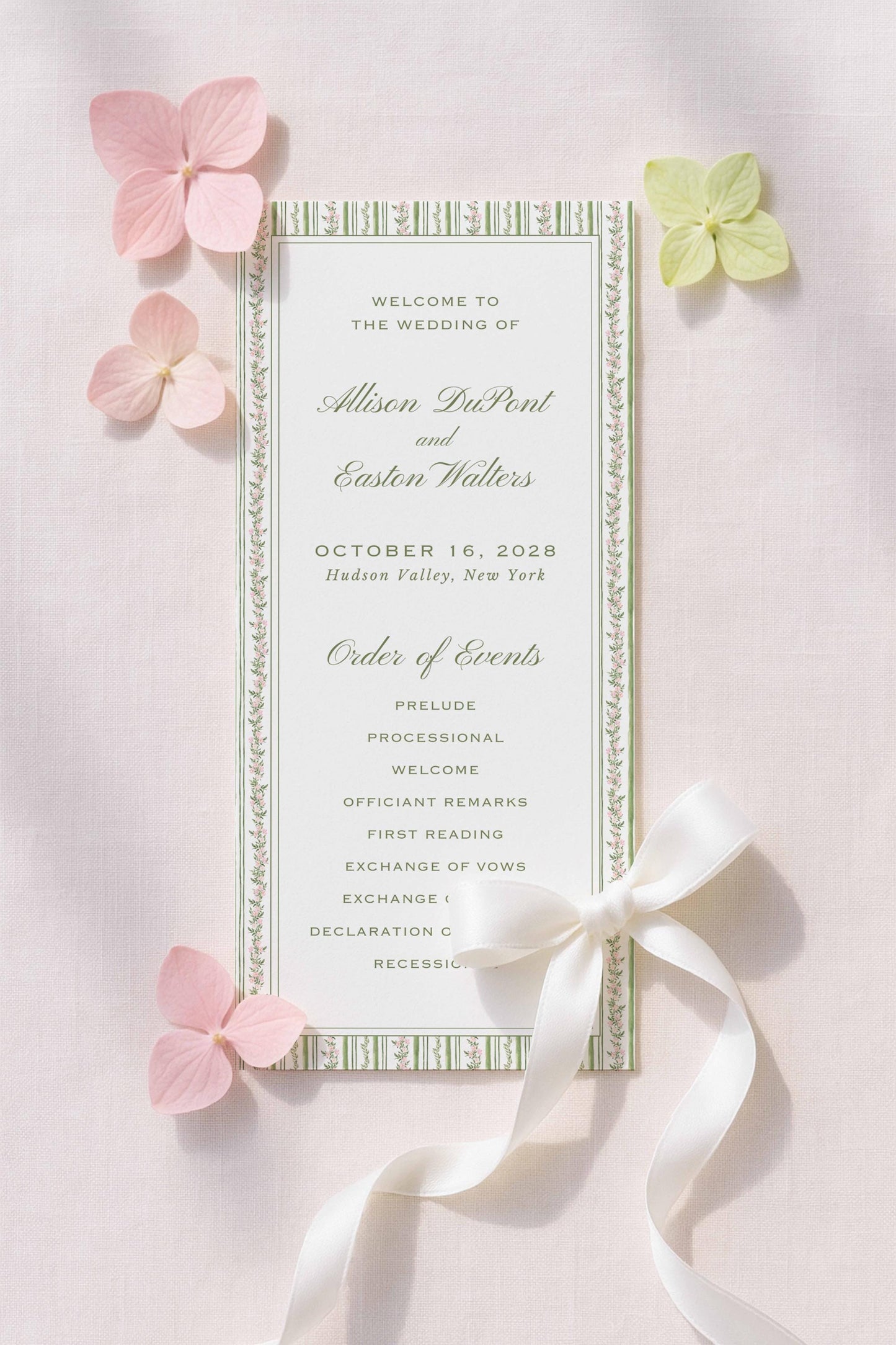 a wedding invitation card with a white ribbon and pink flowers. The card is titled "Welcome to the Wedding of Alison DuPont and Easton Walters" and includes details about the wedding date, location, and order of events.