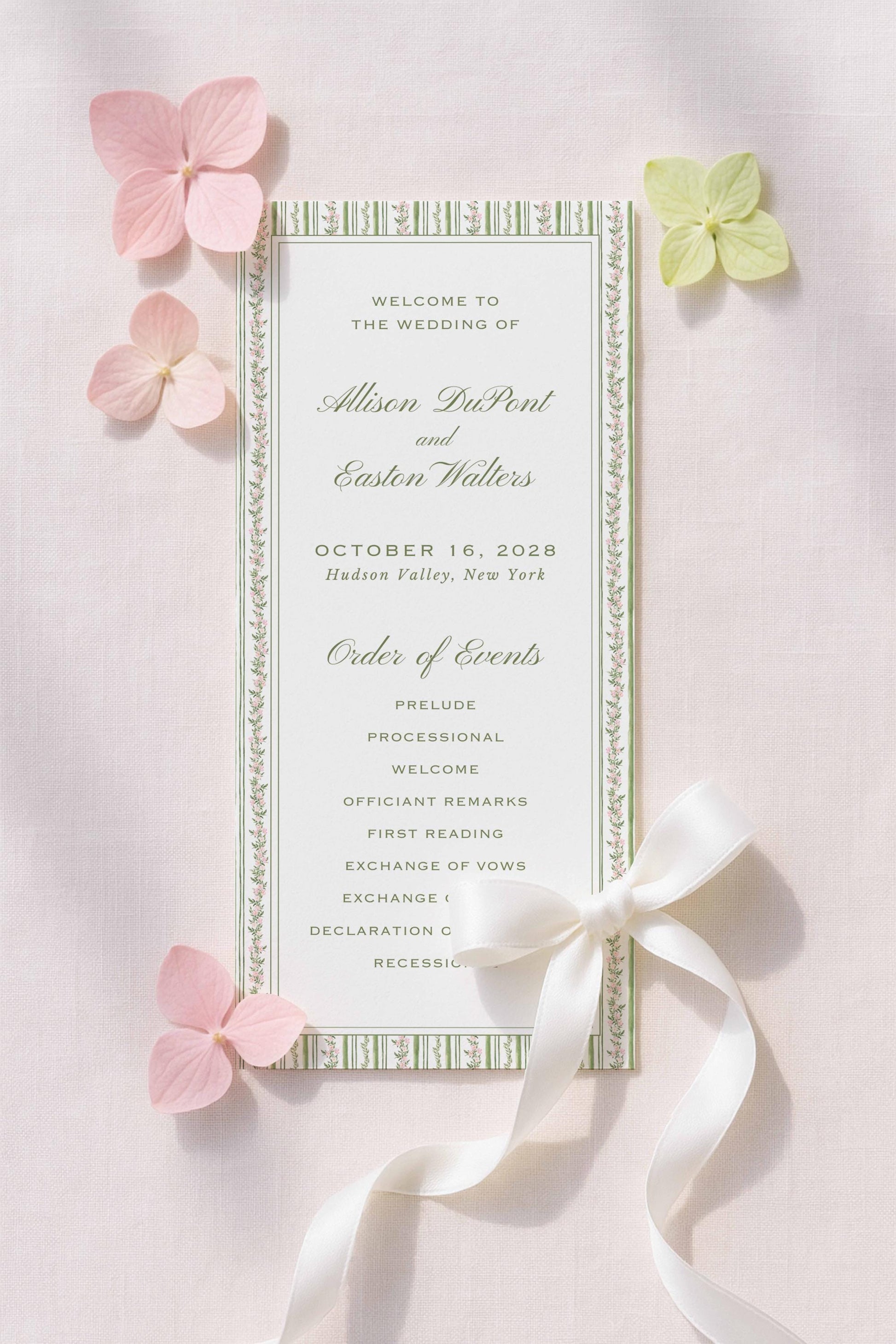 a wedding invitation card with a white ribbon and pink flowers. The card is titled "Welcome to the Wedding of Alison DuPont and Easton Walters" and includes details about the wedding date, location, and order of events.