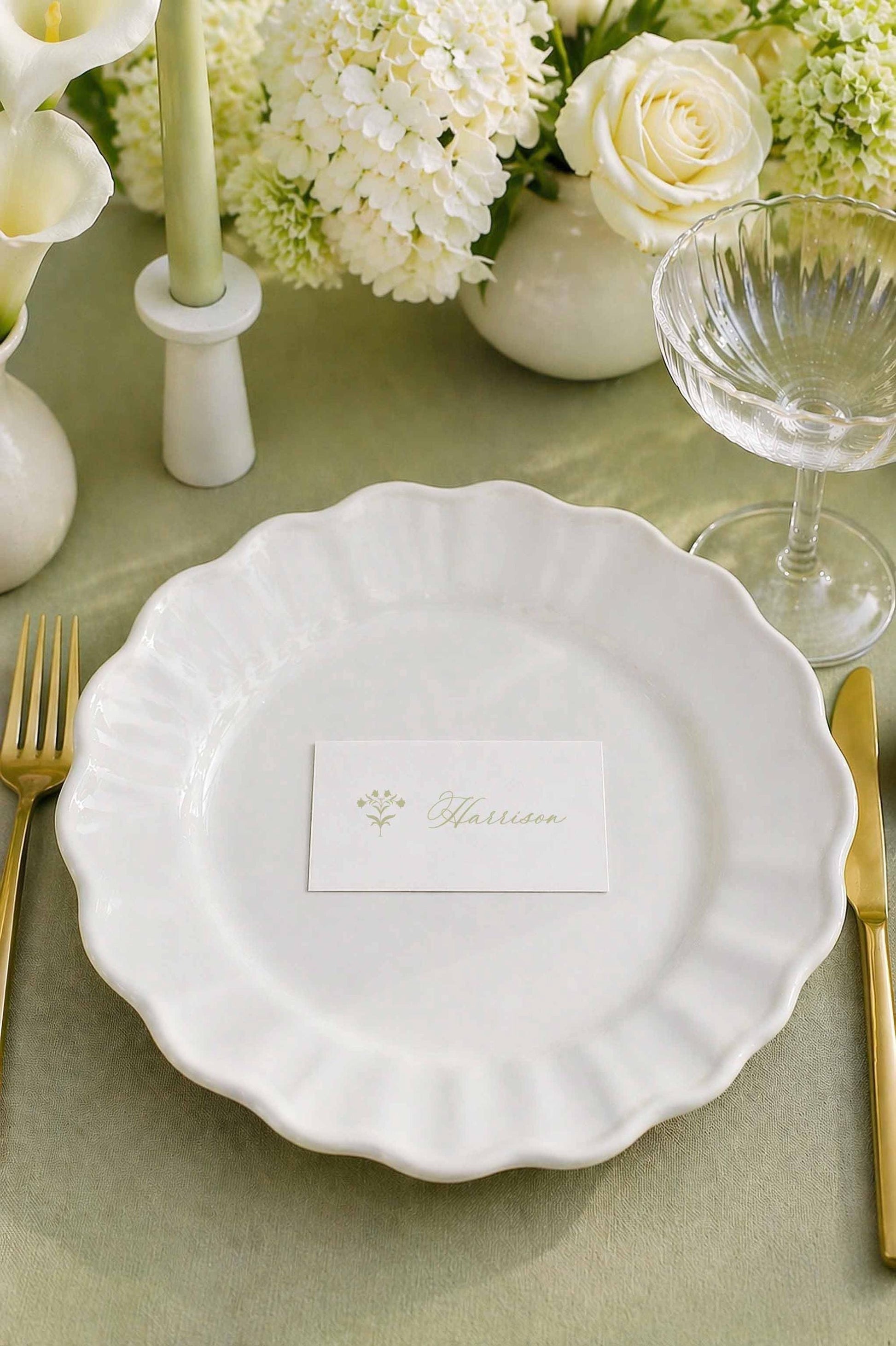 a beautifully set table with a white plate, a name card, a glass of wine, and a vase of white flowers.