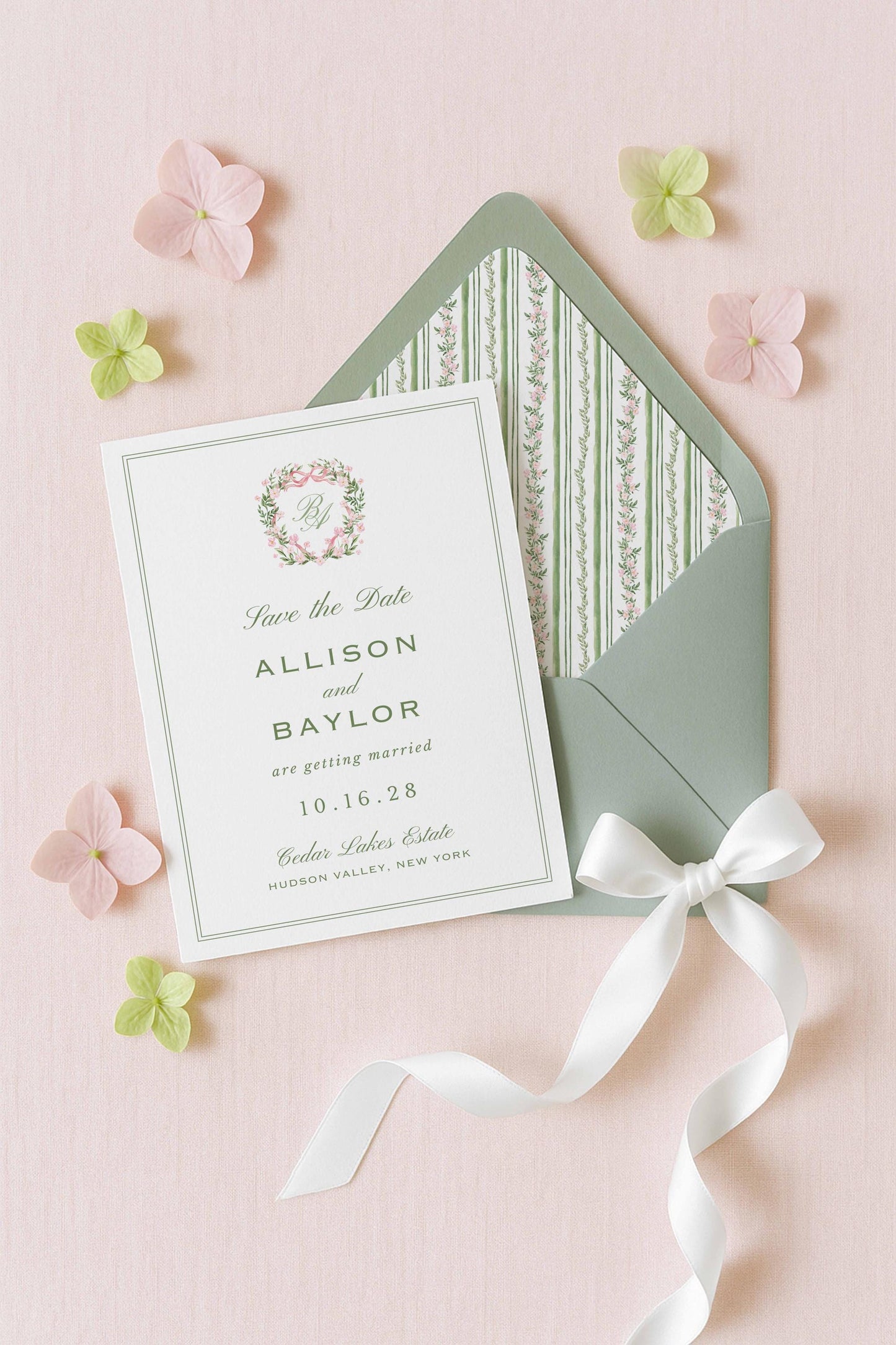 A white wedding invitation card with a green envelope and pink and green flowers on a pink background.