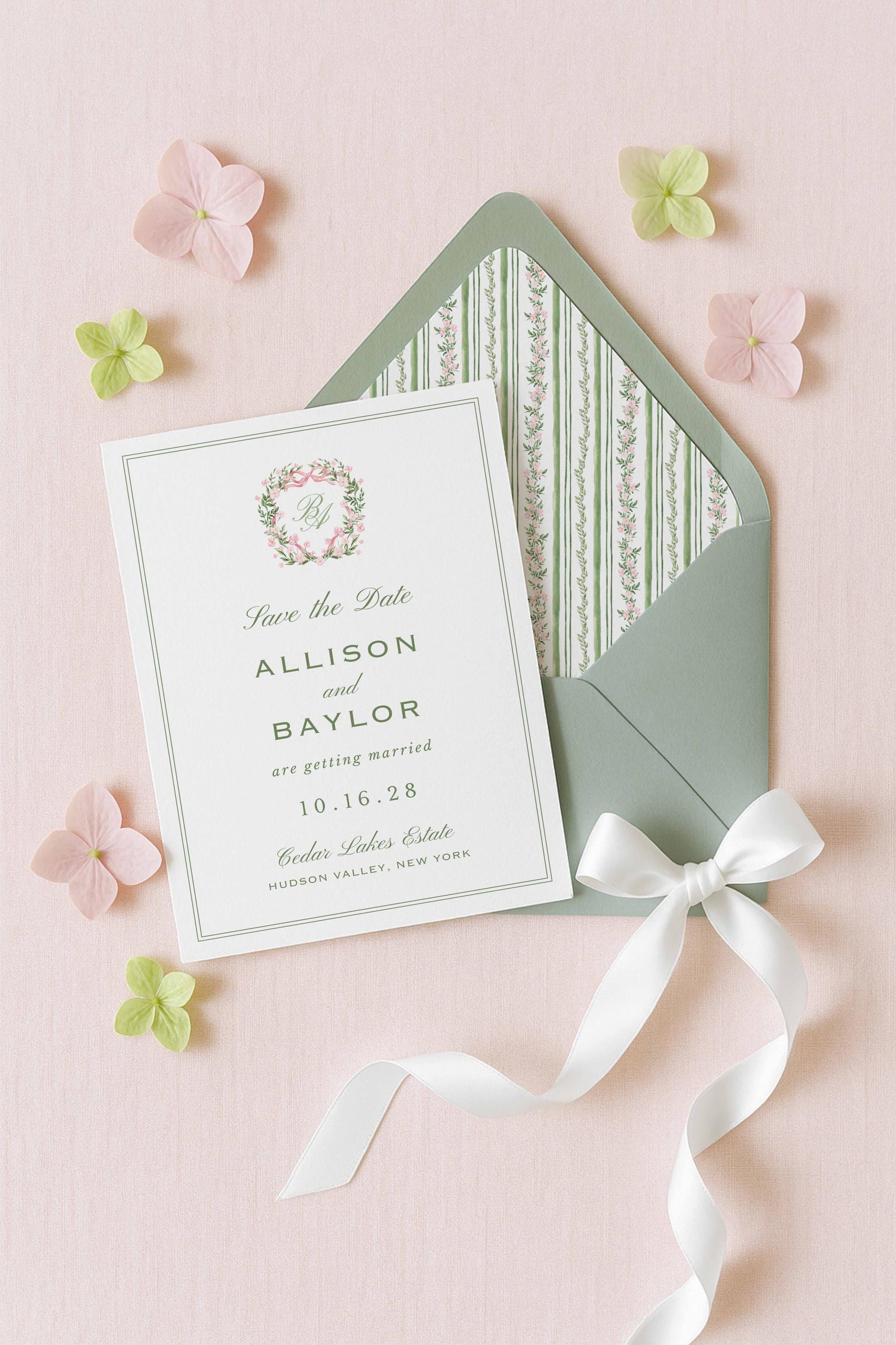 A white wedding invitation card with a green envelope and pink and green flowers on a pink background.