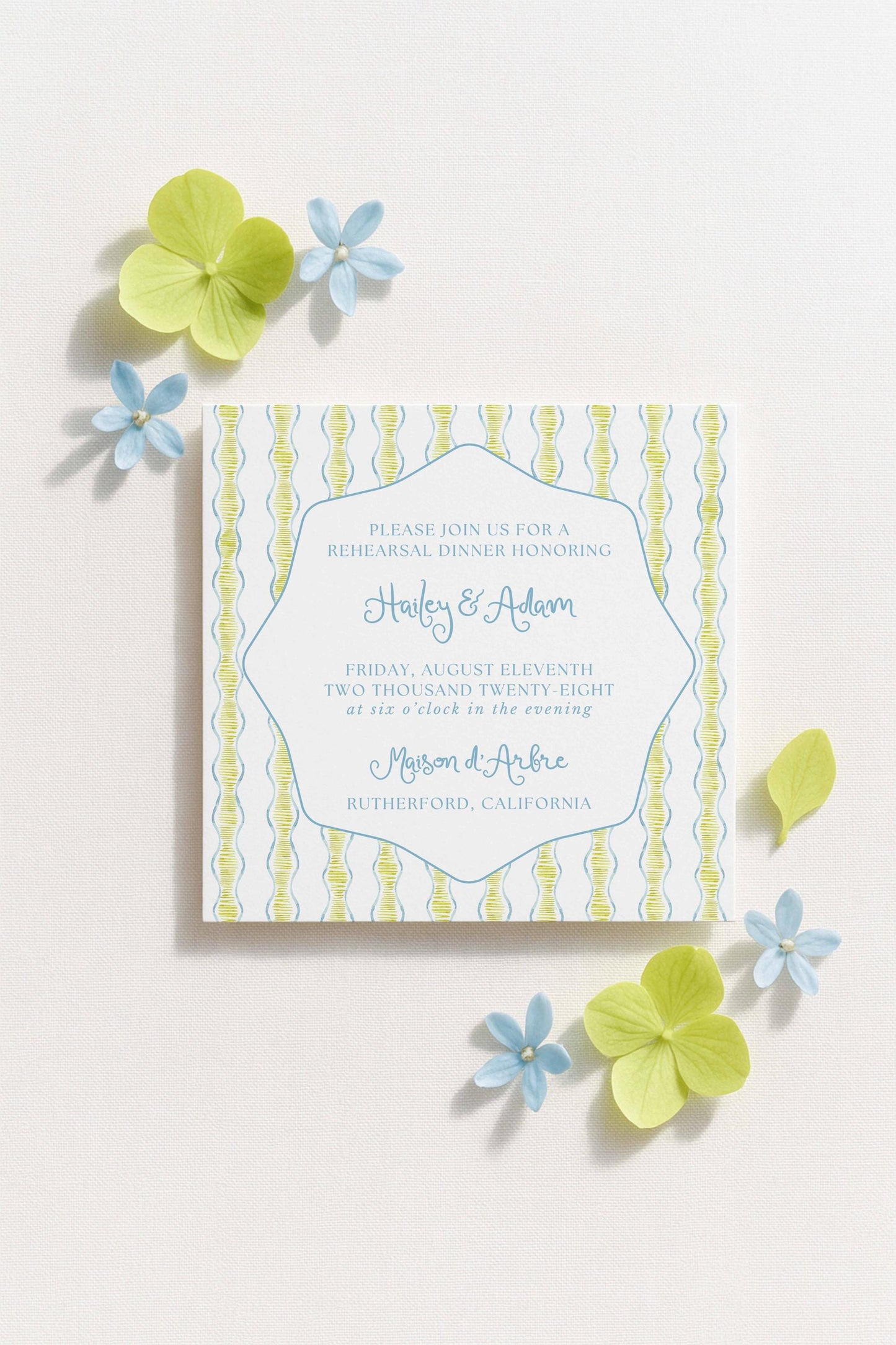 The image is a wedding invitation featuring a blue and white striped pattern, with a floral design and some yellow flowers surrounding it.