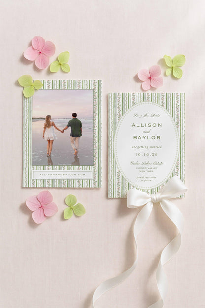 a wedding invitation card with a photo of a couple and a ribbon. The card is placed on a light pink background with pink and green flowers.